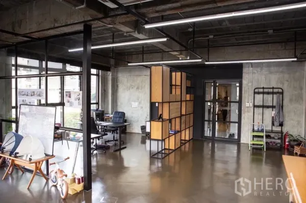 Office Space for rent in Khlong Toei, Bangkok - Modern workspace with exposed ceiling lights, a glass door, large windows, and a modular wood-and-metal divider.