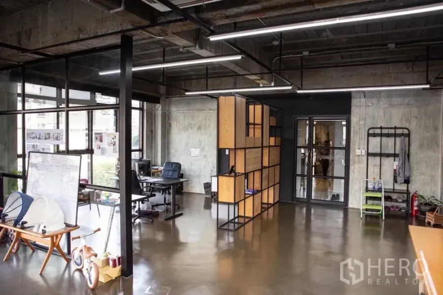 Office Space for rent in Khlong Toei, Bangkok - Modern workspace with exposed ceiling lights, a glass door, large windows, and a modular wood-and-metal divider.