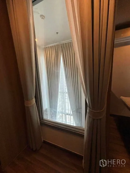 Condominium for rent or sale in Watthana, Bangkok - Interior window with curtains overlooking the double-height living area and tall drapes.