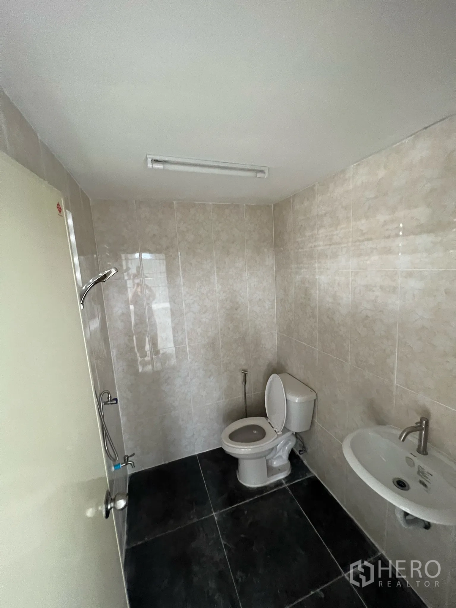 Warehouse for rent in Lam Luk Ka, Pathum Thani - Tiled restroom inside the warehouse with toilet, sink, and handheld spray.
