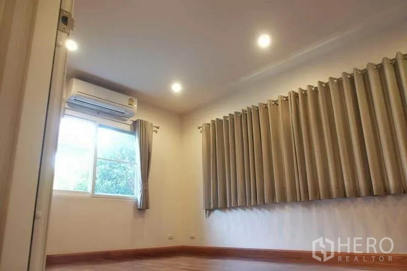 独立式住宅 出租或出售在Pak Kret, Nonthaburi - 明亮房间，配置空调、筒灯与长窗帘，木纹地面。