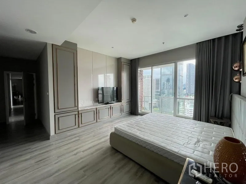 Condominium for sale in Sathon, Bangkok - Spacious master bedroom with custom TV wall, large windows, grey curtains and a city view.