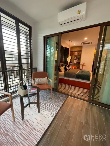 Detached House for sale in Bang Kapi, Bangkok - Covered balcony lounge with seating set, sliding glass doors and wood-look flooring.