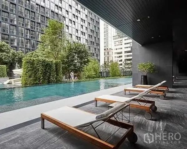 公寓 出租在Pathum Wan, Bangkok - 公寓户外泳池配躺椅，绿化环绕，可见城市高楼景观。