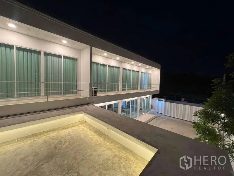 Detached House for rent in Lat Krabang, Bangkok - Contemporary two‑storey facade at night with balcony and illuminated glass walls.