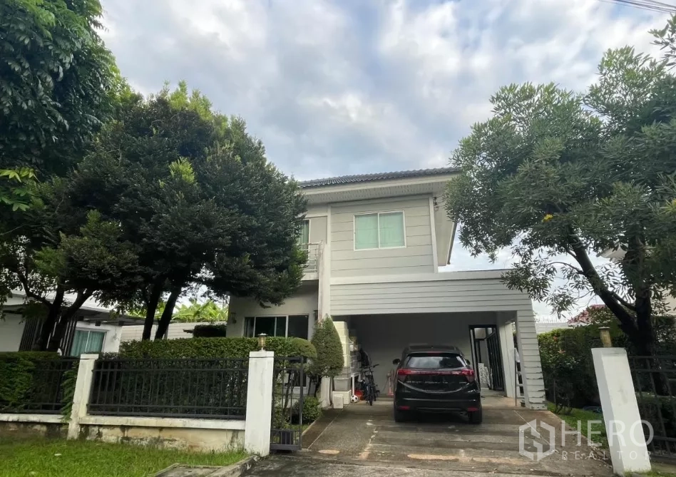 บ้าน ขายในMin Buri, Bangkok - บ้านเดี่ยวสองชั้นพร้อมรั้ว หน้าโครงการมีโรงจอดรถและทางเข้ารถ รายล้อมด้วยต้นไม้ เขตมีนบุรี กรุงเทพฯ