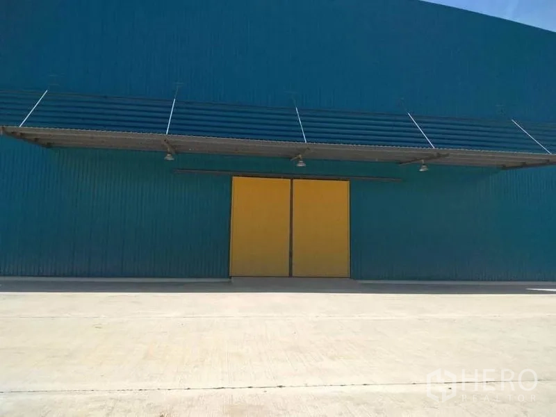 Factory for rent in Mueang Samut Prakan, Samut Prakan - Factory exterior with teal cladding, large yellow sliding doors, canopy and concrete apron.