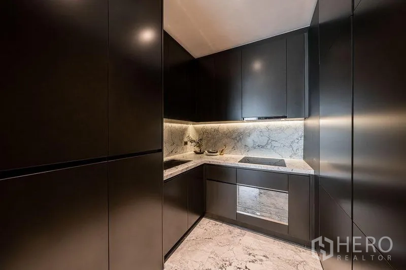 Condominium for rent in Watthana, Bangkok - Sleek U-shaped kitchen with dark cabinetry, marble countertops, and matching backsplash.