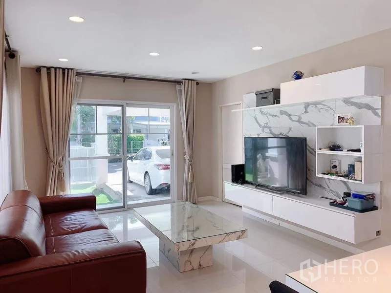 บ้าน ให้เช่าหรือขายในBang Phli, Samut Prakan - ห้องนั่งเล่นมองออกสู่ประตูบานเลื่อนและลานจอดรถ พร้อมสนามหญ้าเล็ก