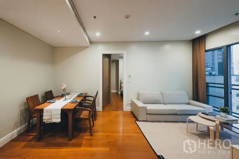 Condominium for rent in Khlong Toei, Bangkok - Dining nook with four-seat wooden table next to living room and balcony doors.
