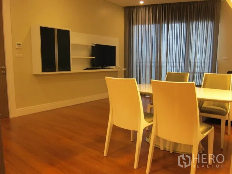 Condominium for rent in Khlong Toei, Bangkok - Dining set facing wall-mounted TV console beside sheer balcony curtains on hardwood floors.