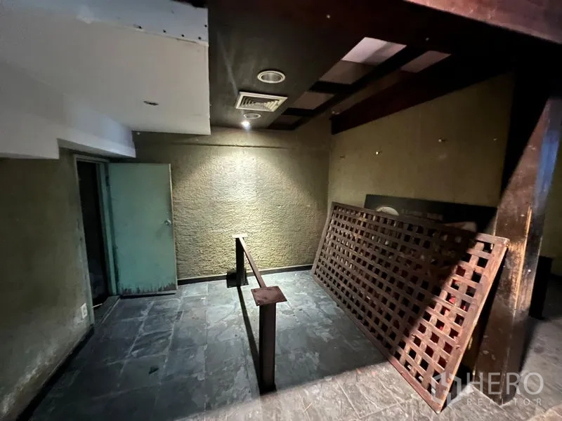 Shophouse for sale in Bang Rak, Bangkok - Raw interior room with textured walls, exposed beams and a wood lattice panel.