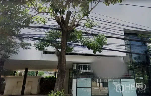 Retail Space for rent in Khlong Toei, Bangkok - Modern low-rise building facade with tall glass windows and roadside trees.