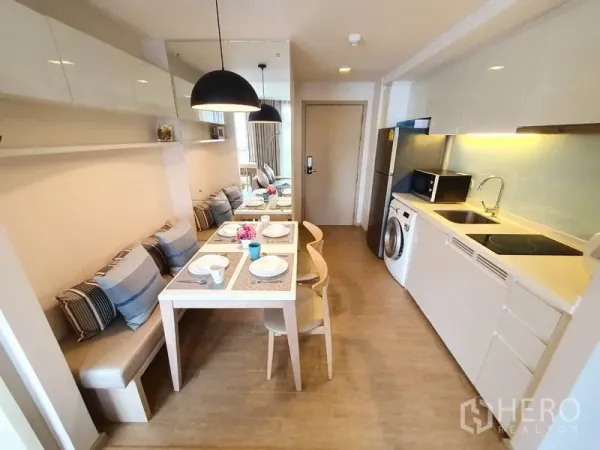 Condominium for rent in Watthana, Bangkok - Compact modern kitchen with white cabinets, sink, cooktop, microwave and in-unit washing machine next to the dining area.