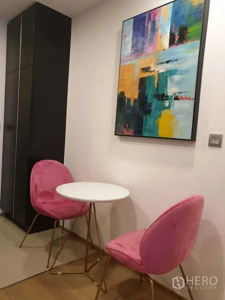 Condominium for rent in Bang Rak, Bangkok - Small dining corner with two pink chairs and abstract art.