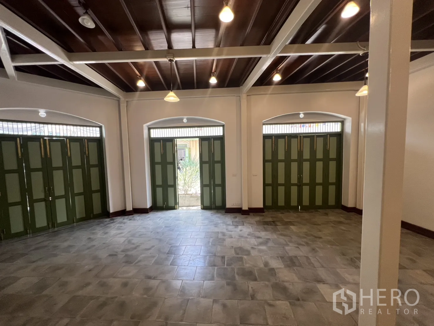 店屋 for rent in Samphanthawong, Bangkok - 一层营业厅，层高充裕，外露梁架与吊灯，三扇宽大的绿色折叠店门。