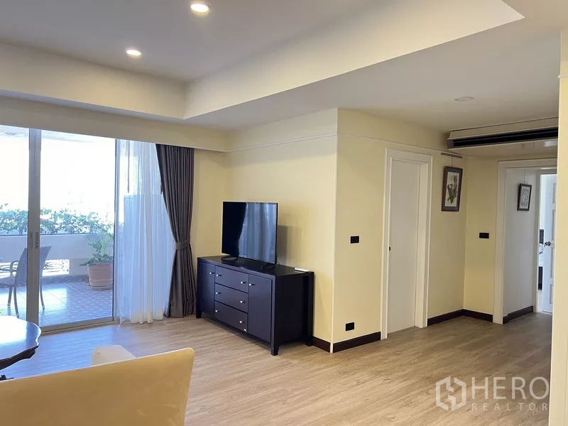 Condominium for rent in Khlong Toei, Bangkok - Open-plan lounge with recessed lights, wood floors and access to a large covered balcony beside a TV stand.