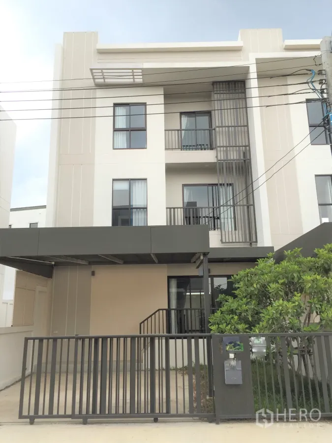 Townhouse for rent in Saphan Sung, Bangkok - Modern three-storey townhouse facade with gated carport, balconies and small front tree.