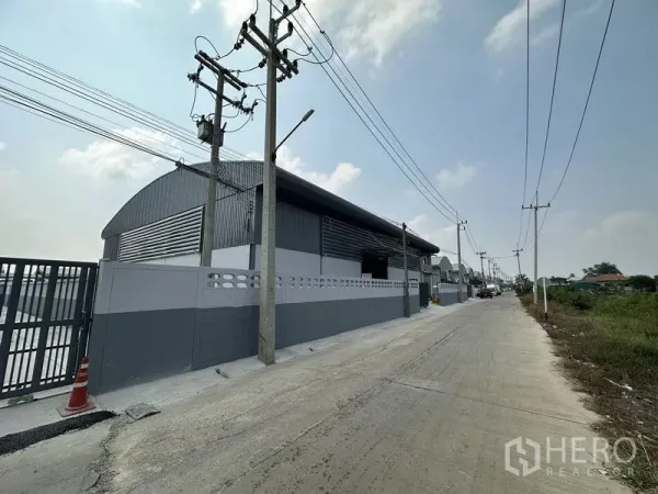 โรงงาน ให้เช่าในPathum Thani - ถนนหน้าโครงการ เห็นกำแพงรั้วโรงงานและประตูทางเข้าบนถนนอุตสาหกรรมเงียบสงบ