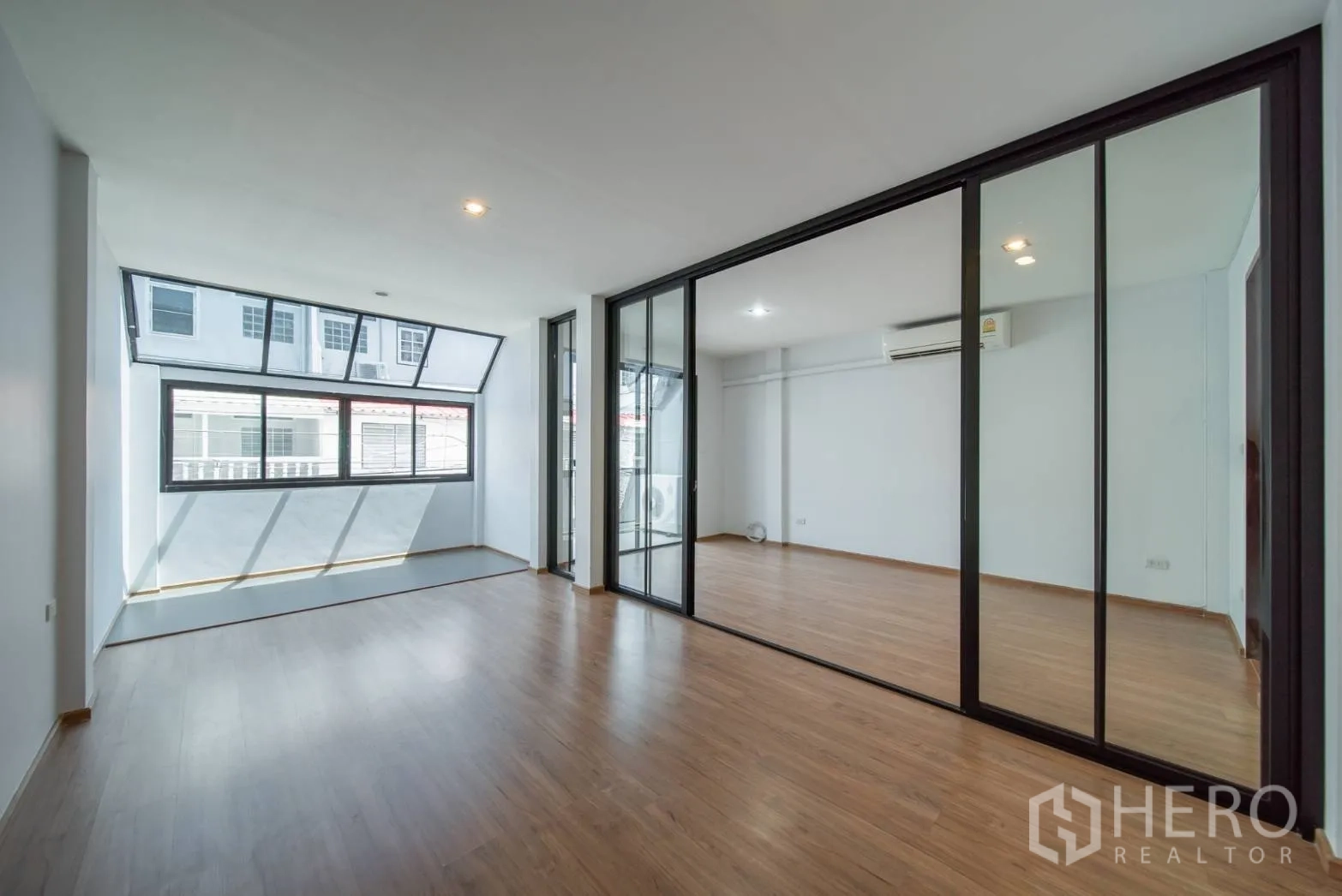 Townhouse for rent in Watthana, Bangkok - Empty room with wood floors, glass partition and wide windows for natural light.