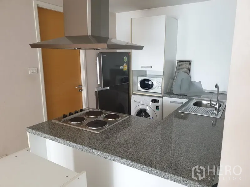 Condominium for rent or sale in Watthana, Bangkok - Modern open kitchen with granite countertop, electric cooktop and hood, fridge, sink and in-unit washer.
