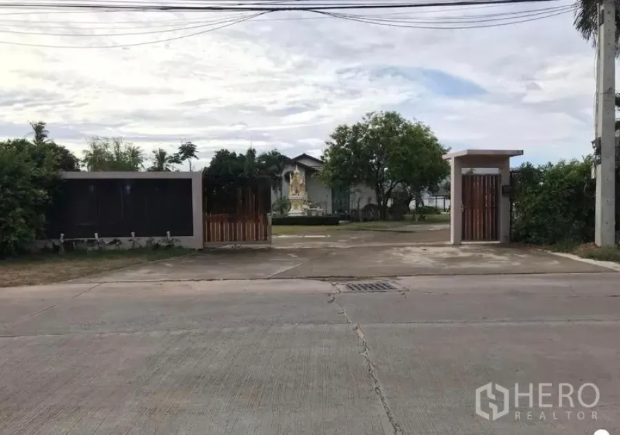 Warehouse for sale in Chon Buri - Street-facing main gate and guard entrance of the property with power lines overhead.
