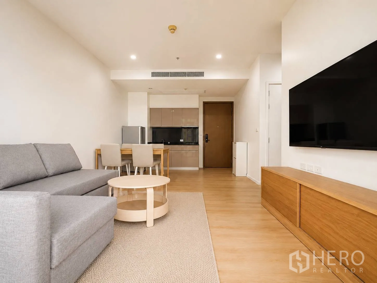 คอนโด for rent or sale in Watthana, Bangkok - ห้องนั่งเล่นแบบโอเพ่นพร้อมโซฟาสีเทา โต๊ะกาแฟทรงกลม ชุดทานข้าว ครัวแพนทรี และทีวีติดผนังบนพื้นไม้