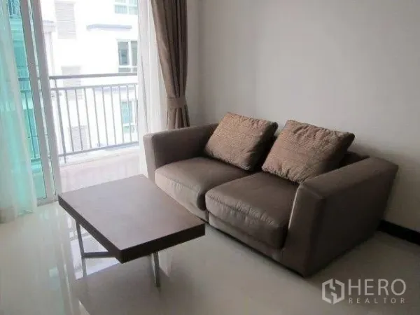 Condominium for rent in Khlong Toei, Bangkok - Two-seat sofa and low coffee table next to balcony doors with an urban outlook.