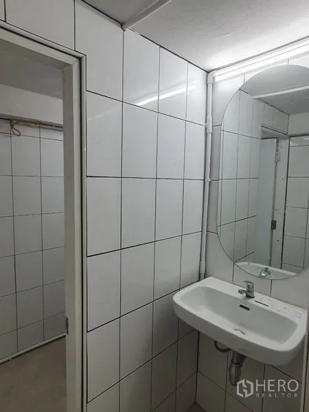 Shophouse for rent in Phra Khanong, Bangkok - Compact bathroom with white tiled walls, wall-hung sink and round mirror.