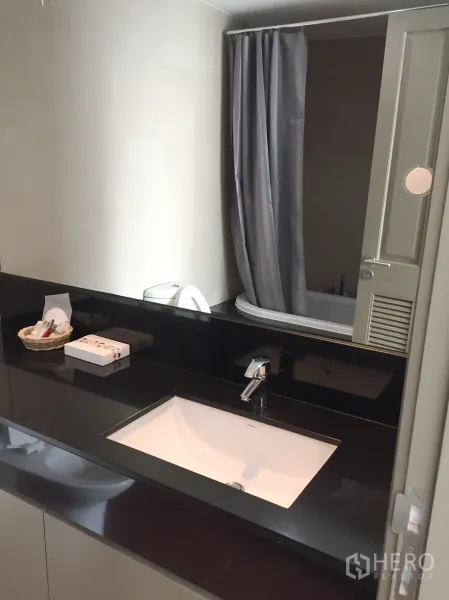 คอนโด ให้เช่าในPathum Wan, Bangkok - ห้องน้ำสมัยใหม่ เคาน์เตอร์สีดำ อ่างล้างหน้า กระจก และอ่างอาบน้ำพร้อมผ้าม่าน