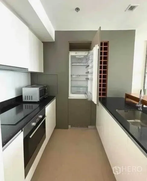 Condominium for rent in Khlong San, Bangkok - Modern galley kitchen with black stone countertops, oven, microwave, wine rack and an open refrigerator.