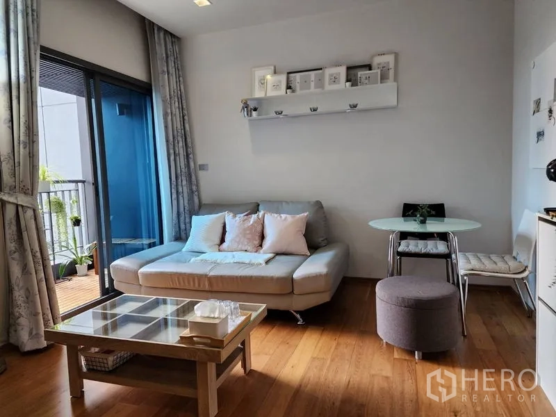 Condominium for rent in Watthana, Bangkok - Living room toward the balcony with sofa, ottoman and small dining set.