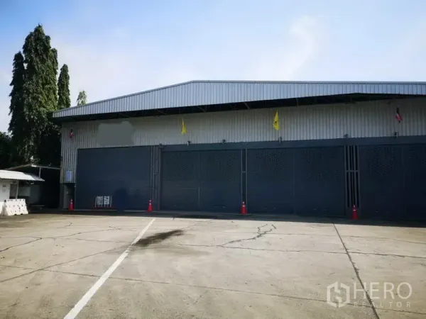 คลังสินค้า ให้เช่าในPak Kret, Nonthaburi - ด้านหน้าโกดังผนังเมทัลชีท ประตูบานใหญ่หลายช่อง พร้อมลานคอนกรีตกว้างสำหรับรถบรรทุก