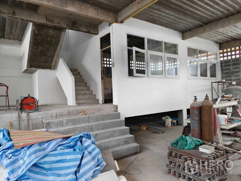 Warehouse for rent in Phra Khanong, Bangkok - Mezzanine office with windows and concrete stairs inside a partially renovated warehouse.