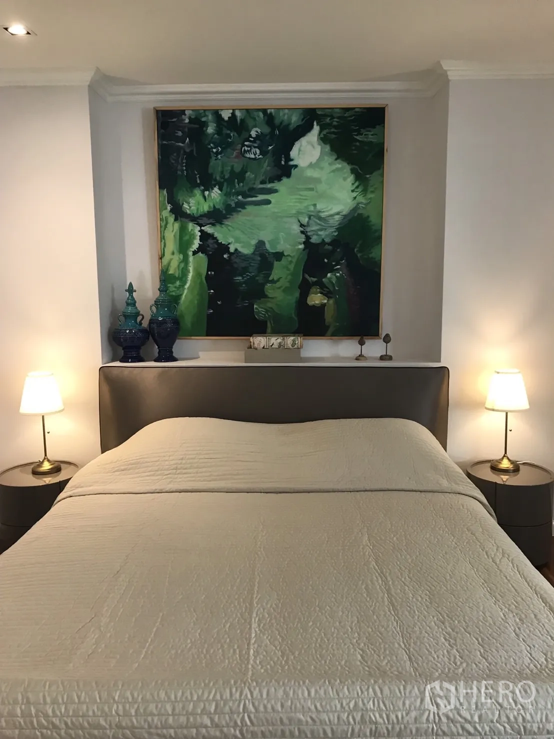 Condominium for rent in Bangkok - Cozy bedroom with upholstered headboard, bedside tables, lamps and large green artwork.