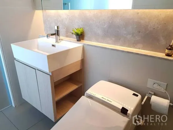 Condominium for rent in Khlong Toei, Bangkok - Modern bathroom featuring a square-basin vanity, bidet toilet and backlit shelf.