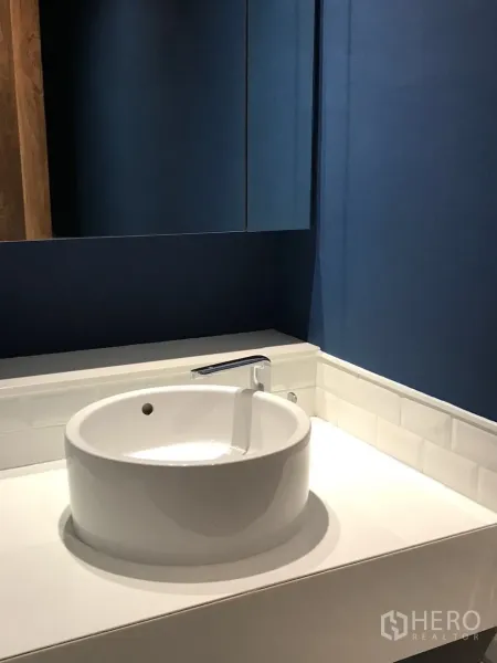 Condominium for rent in Khlong Toei, Bangkok - Powder room featuring a deep blue accent wall and round countertop basin.