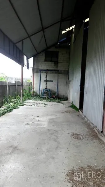Warehouse for sale in Pathum Thani - Covered side loading bay with concrete floor beside corrugated metal wall and boundary fence.
