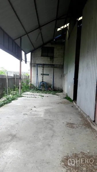 Warehouse for sale in Pathum Thani - Covered side loading bay with concrete floor beside corrugated metal wall and boundary fence.