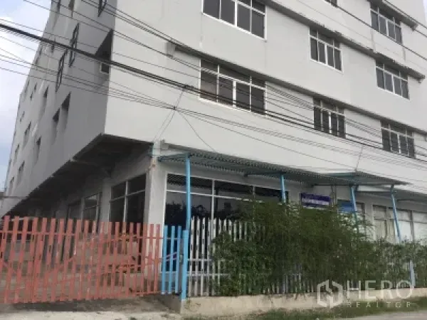 อาคารพาณิชย์ ให้เช่าในLam Luk Ka, Pathum Thani - ตึกแถวมุมอาคารสีเทา หน้ากระจกกว้าง มีกันสาดสีน้ำเงินและรั้วโลหะ ในย่านลำลูกกา ปทุมธานี