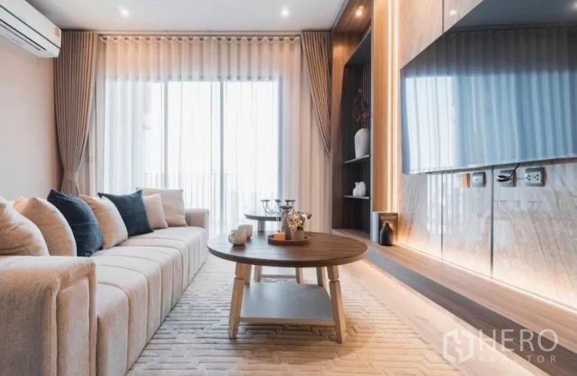 Condominium for rent in Watthana, Bangkok - Living room with large sofa, coffee table and TV wall beside balcony doors.