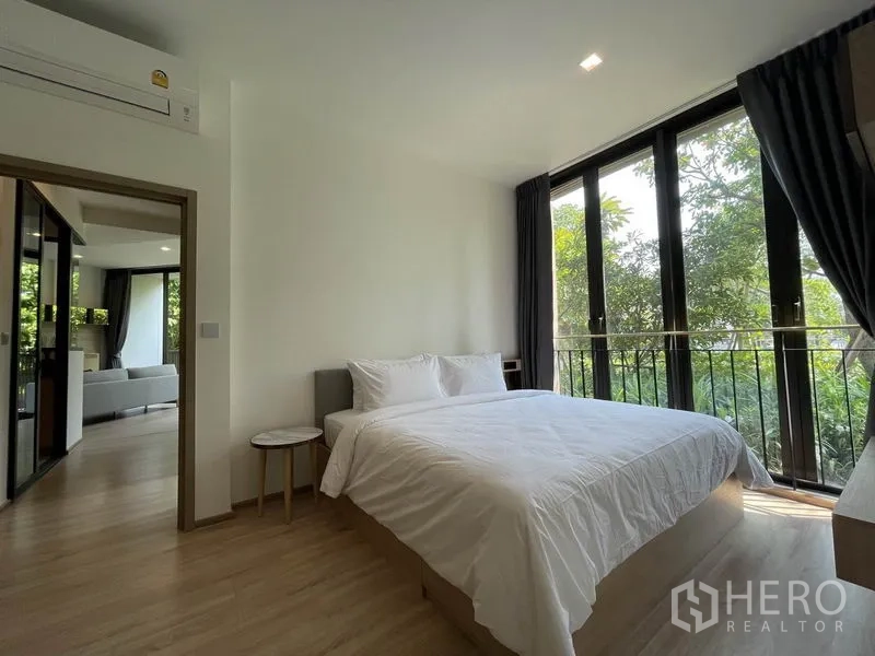 Condominium for sale in Watthana, Bangkok - Bedroom with white bedding and large windows, looking back toward the living area.