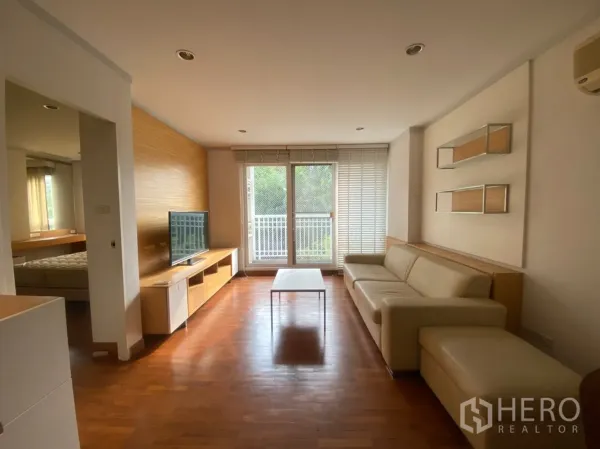 Condominium for rent or sale in Sathon, Bangkok - Living area with L-shaped sofa opening to a balcony with a green view.