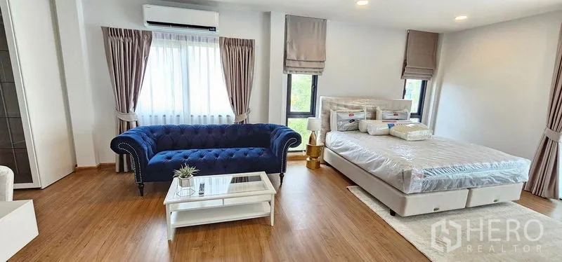 Detached House for rent in Bang Phli, Samut Prakan - Spacious master bedroom with blue velvet sofa, queen bed, wood flooring and large windows.
