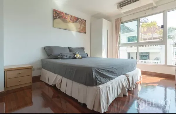 Detached House for rent in Phra Khanong, Bangkok - Sunlit bedroom with large corner windows, wood floors and a double bed.
