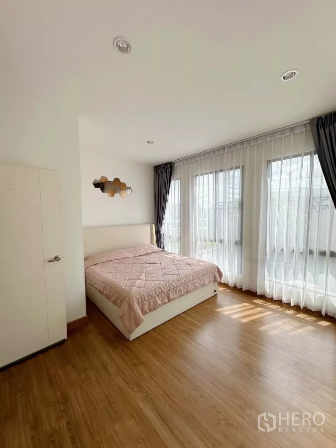 联排别墅 出租在Bang Phli, Samut Prakan - 主卧木地板，转角落地窗与轻薄窗帘，采光充足。