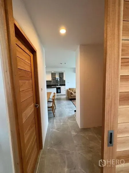 Condominium for rent or sale - Hallway with wooden doors leading to an open-plan living and kitchen area in a modern condo.