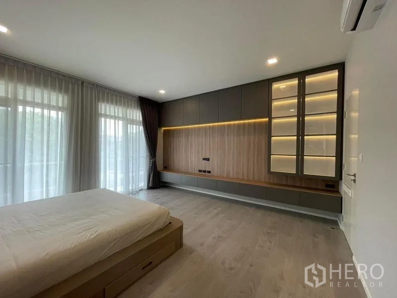 Detached House for rent in Prawet, Bangkok - Master bedroom wall of custom built‑ins with illuminated display shelves and warm wood accents.