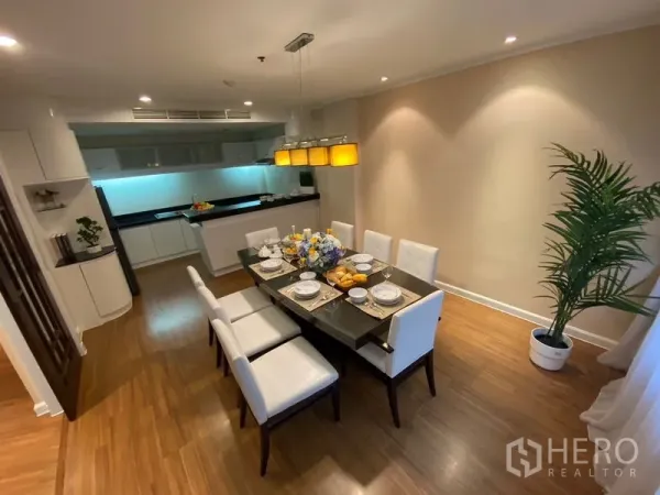 Apartment for rent in Watthana, Bangkok - Dining room with an eight-seat table, pendant lights and an open kitchen in an Ekkamai-area apartment.