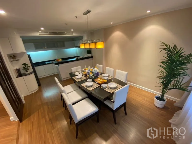 Apartment for rent in Watthana, Bangkok - Dining room with an eight-seat table, pendant lights and an open kitchen in an Ekkamai-area apartment.
